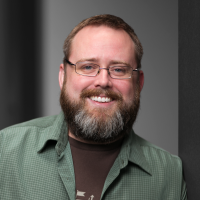 Headshot of Adam Wilbert, a dapper man with a graying beard